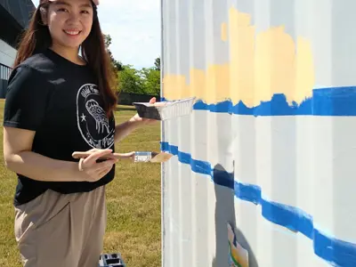 Woman smiling and holding paint brush while painting storage container