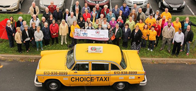 Large group of volunteers stand behind Choice Taxi vehicle
