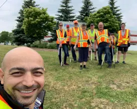 A smiling man standing in front of a group of people who are wearing orange vests.