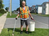An Adopt a Street volunteer holding a picker and a bucket. He is seen wearing an orange vest.
