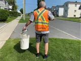 A man wearing an orange volunteer vest and holding a picker and a bucket