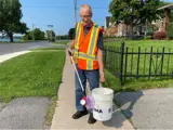 A man wearing an orange vest, holding a picker and a bucket.