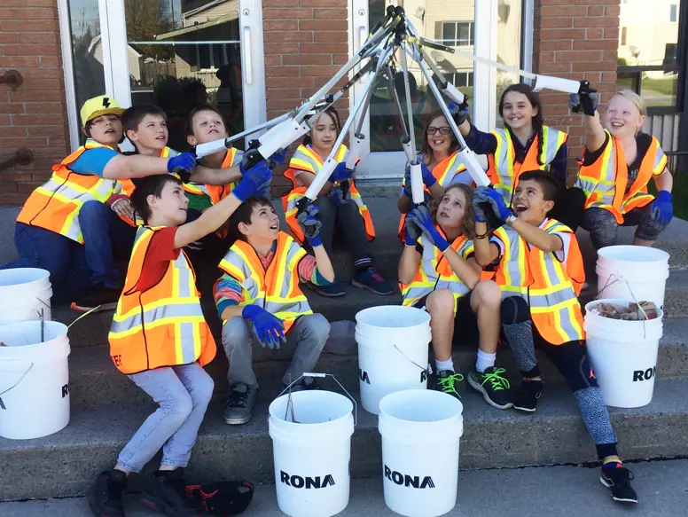 Smiling children point their litter pickers in the air.