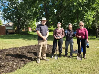 Four people standing in front of an unplanted garden bed holding shovels