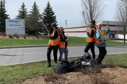 Four volunteers standing over bags of garbage that they picked up around the Walmart warehouse.